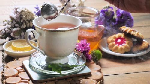 Black tea in a light cup on a table, against a light background, is brewed using a metal strainer.