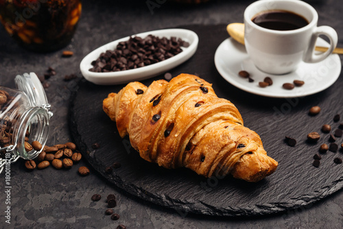 A large airy croissant with chocolate on a dark background tempts coffee