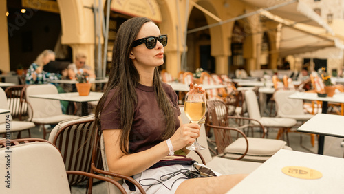 Beautiful woman enjoying a glass of wine seated in a very pleasant outdoor setting. Relaxing atmosphere, sunny day, and leisure lifestyle moment.
