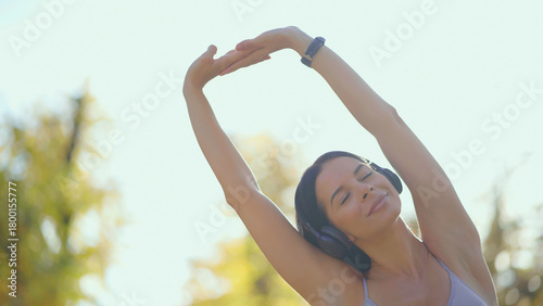 Foto Young woman wearing headphones performing yoga stretches with eyes closed, enjoy