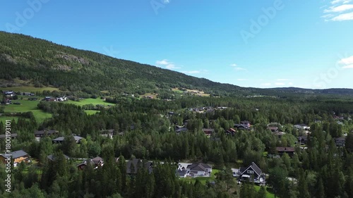 Drone flying over houses in Norway, revealing surrounding mountains and dense green trees in a peaceful natural landscape.