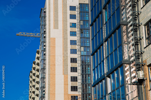 Modern residential buildings are being built with cranes in the foreground against a bright blue sky, highlighting the city's growth and construction activity. High quality photo