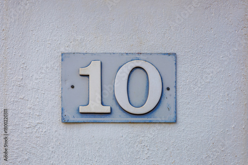 Fototapeta Naklejka Na Ścianę i Meble -  Retro style traditional nameplate with figures of one and zero. 10 plaque. Enamel house number ten on old light shabby wall. Architectural details. Crete, Greece