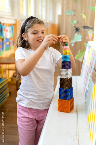 Child builds a tower of beads cubes according to the Montessori method. Alternative education for studying mathematics, algebra, geometry, arithmetic in elementary school.