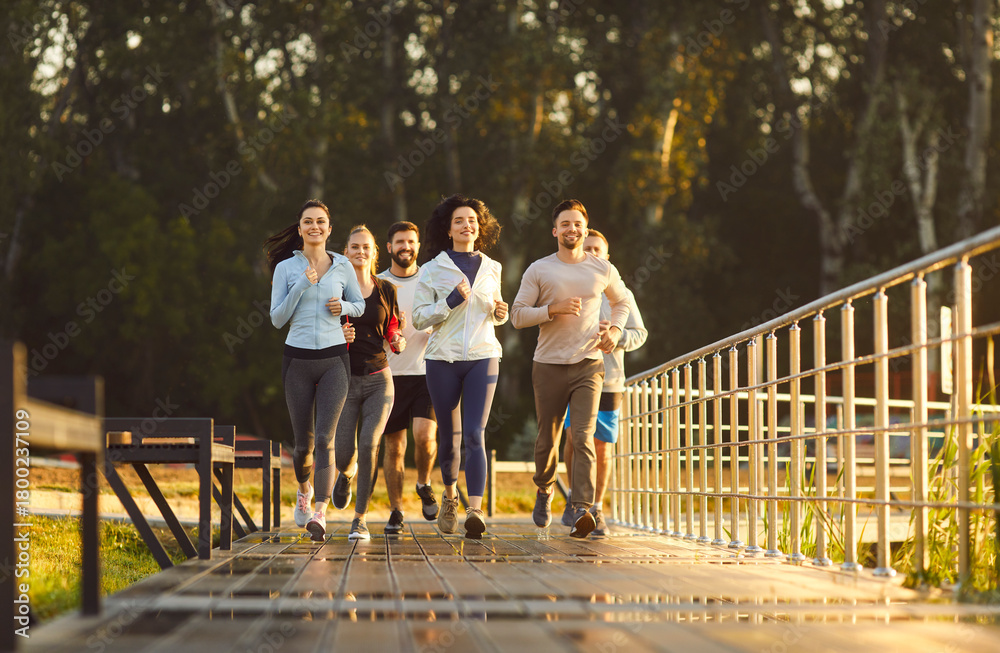Fototapeta premium Runners group jogging in park together in outdoor fitness workout. Fit people training endurance in exercises and marathon in summer morning, team of athletes running race on bridge with smiles