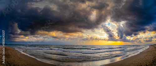 Fototapeta Naklejka Na Ścianę i Meble -  Dramatic sunset over sandy beach with dark storm clouds and breaking waves, capturing the moody atmosphere of changing autumn weather. Evrenseki, Antalya, Turkey.

