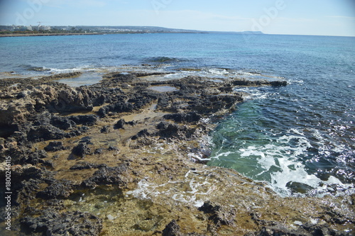 Rocky coastline with clear water and gentle waves under bright blue sky, picturesque coastal nature, copy space