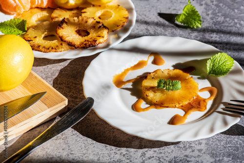 Grilled pineapple slices arranged with fresh mandarin segments and lemon pieces, creating a vibrant and refreshing tropical composition. The caramelized edges of the pineapple add warmth and texture, 