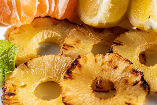 Grilled pineapple slices arranged with fresh mandarin segments and lemon pieces, creating a vibrant and refreshing tropical composition. The caramelized edges of the pineapple add warmth and texture, 