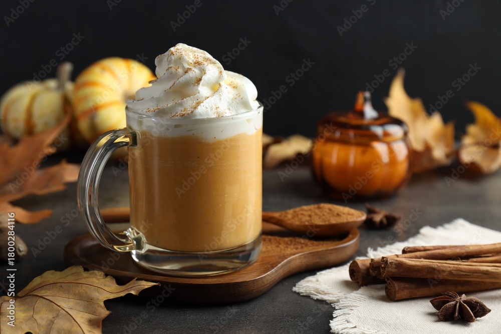 Obraz premium Tasty pumpkin latte with whipped cream in glass cup, spices and autumn decor on grey table, closeup
