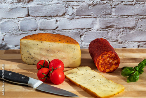 Sliced kulen and semi-hard cheese arranged neatly on a plate, garnished with fresh basil leaves. The vibrant colors of the red cured sausage, creamy-yellow cheese, and green basil create a visually ap