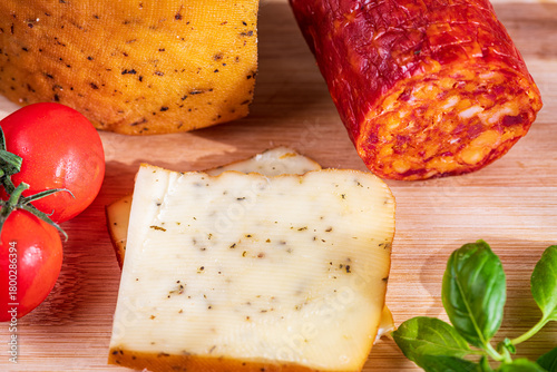 Sliced kulen and semi-hard cheese arranged neatly on a plate, garnished with fresh basil leaves. The vibrant colors of the red cured sausage, creamy-yellow cheese, and green basil create a visually ap