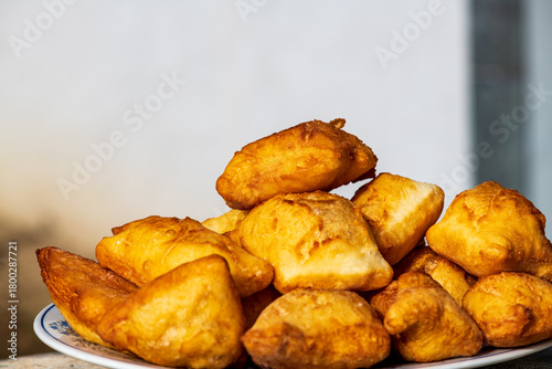Golden, freshly fried fritters arranged on a plate, featuring a crispy exterior and a soft, airy inside. Warm lighting enhances their rich golden color and homemade rustic appearance. 