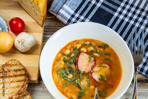A hearty bowl of cooked bean stew with tender pieces of meat, served in a clean white dish. The warm, rich broth highlights the soft beans and juicy meat, while natural lighting 