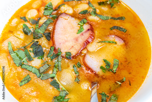 A hearty bowl of cooked bean stew with tender pieces of meat, served in a clean white dish. The warm, rich broth highlights the soft beans and juicy meat, while natural lighting 