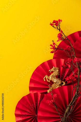 Fototapeta Naklejka Na Ścianę i Meble -  Golden horse statue on a red paper fan background with red plum blossoms against a bright yellow background. Ideal for Chinese New Year, year of the horse, or fortune themes.