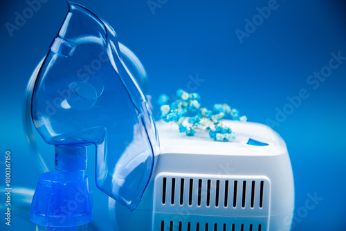 Close-up side view of a blue mask and a device on a blue background and flowers nearby. The concept of treating respiratory diseases, lung diseases, prevention and self-care. High quality photo