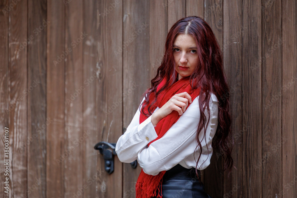 Fototapeta premium Young woman posing in front of wooden door with red scarf