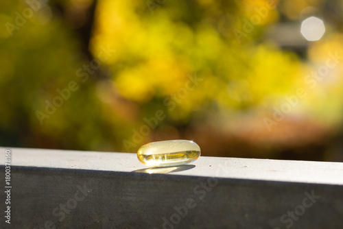 Closeup of a vitamin D 3 capsule against colourful trees in fall.