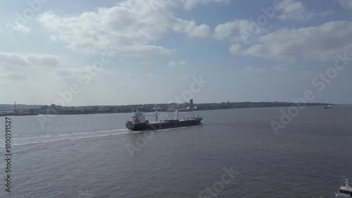 Cargo ship sails smoothly along the river in bright daylight in Liverpool.