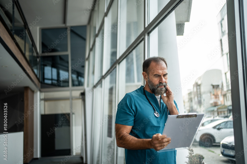 Fototapeta premium Serious doctor reviewing medical record in hospital