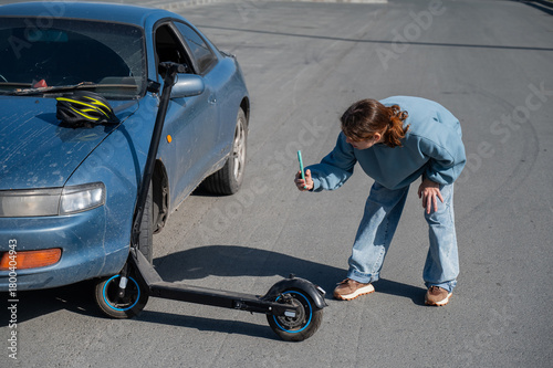 Woman examines and photographs the damage caused by a collision between an electric scooter and a car.