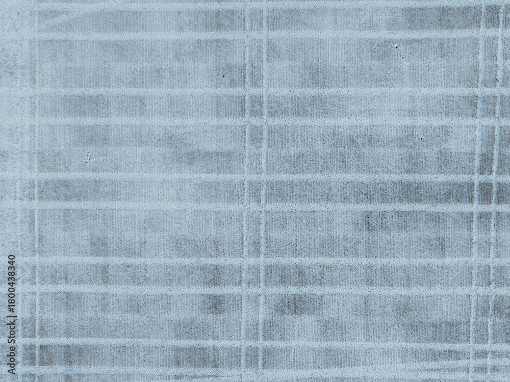 Fototapeta premium Aerial top-down drone view of a snowy field in Estonia, with distinctive tractor tracks creating abstract lines in the fresh snow.