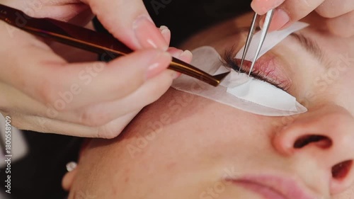 A young cosmetologist carefully glues eyelashes with tweezers.