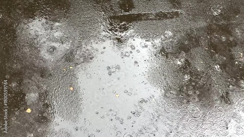 Raindrops on asphalt, viewed from above. A view of an asphalt road during a light rain shower on a cloudy day.