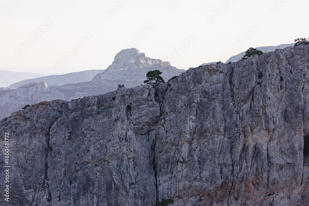 Fototapeta premium Rocky mountain cliffs near Tarragona, Spain, with a lone tree growing on the ridge and layered peaks in soft evening light.
