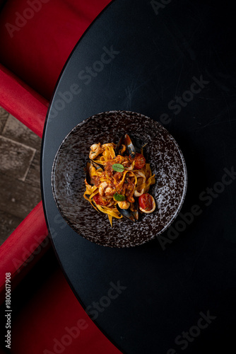 A beautifully arranged plate of seafood pasta showcases vibrant colors and textures. Set against a simple black table, the dish invites a feast for the senses in an intimate setting