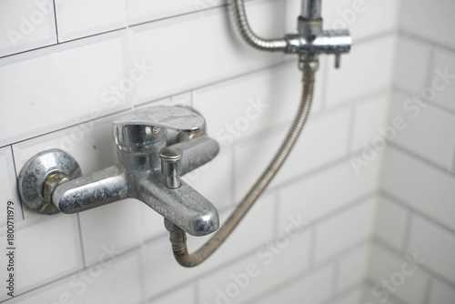 Old, corroded shower mixer tap with limescale buildup on white subway tiles. Reflects plumbing issues, hard water damage, and renovation needs.
