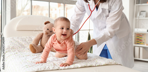 Female pediatrician listening to little baby on couch in clinic