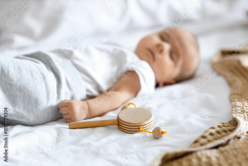 Cute little baby with rattle sleeping on bed at home