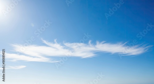 Fototapeta Naklejka Na Ścianę i Meble -  A serene blue sky with wispy white clouds and a bright sun shining down.