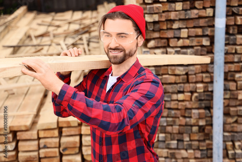 Tableau sur toile Male carpenter carrying wooden plank at sawmill