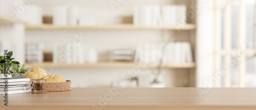 Fototapeta Naklejka Na Ścianę i Meble -  Coffee and breads aside potted plant on wooden counter table across bookshelf in blurred living room
