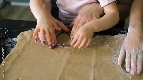 Close-up of hands from a mother and her daughters pressing and shaping ginger cookie dough, highlighting the shared learning and warm family participation in homemade baking concept