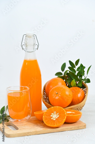 Freshly squeezed orange juice in a glass, a full bottle, and an arrangement of whole and sliced oranges against a white background.
