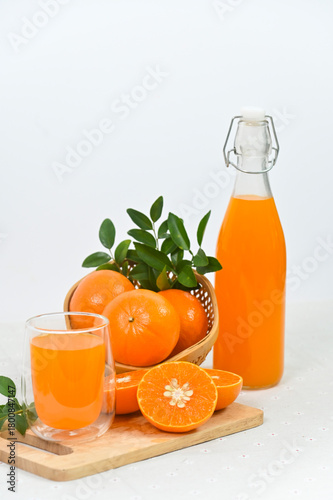 Freshly squeezed orange juice in a glass, a full bottle, and an arrangement of whole and sliced oranges against a white background.