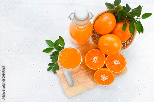 An overhead view captures a glass of freshly squeezed orange juice, a bottle of fresh juice, and whole and halved oranges arranged on a white background.