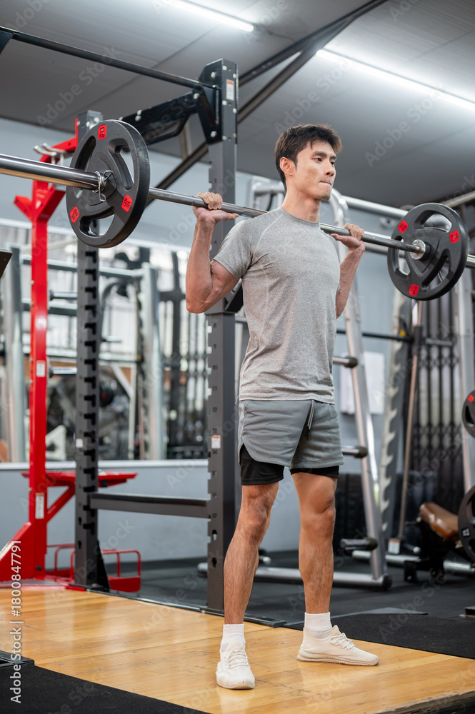 Fototapeta premium Asian man client in sportswear standing and exercising with barbell weight lifting equipment in gym.