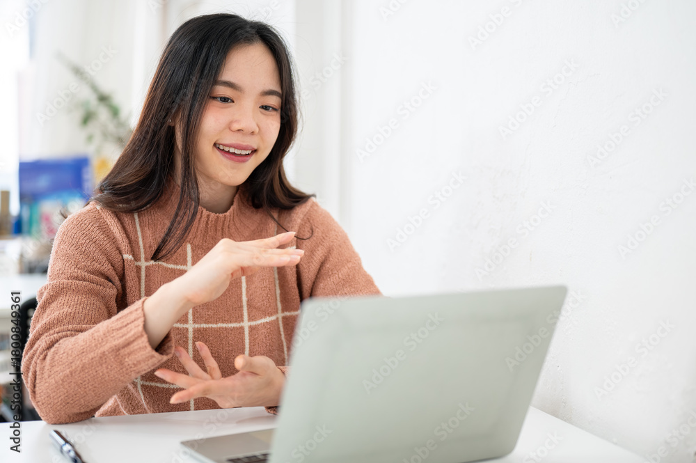 Obraz premium Asian woman explaining with hands and looking at a laptop on table in white room at office or cafe.