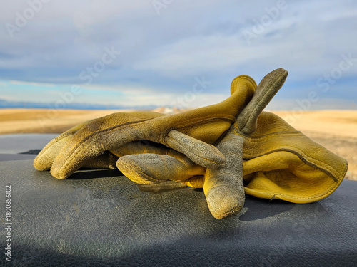 Yellow leather work gloves with distressed and worn fingers sitting on the dashboard of a vehicle.
