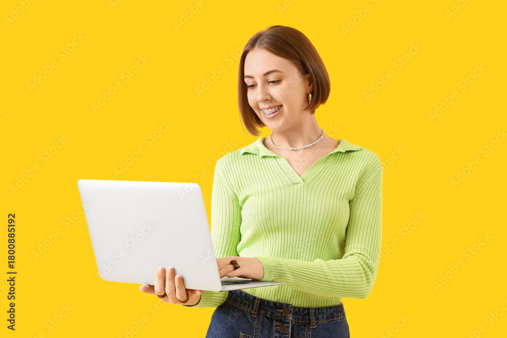 Naklejka premium Young woman with dental braces using laptop on yellow background