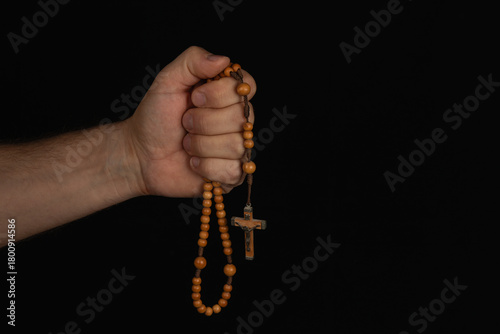 Hand holding wooden rosary with crucifix against dark background