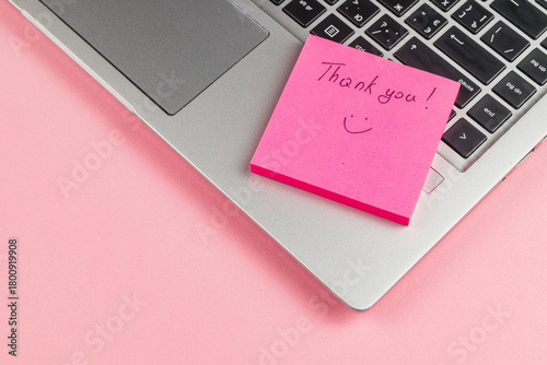 Thank you note on pink sticky pad next to laptop on a pink background