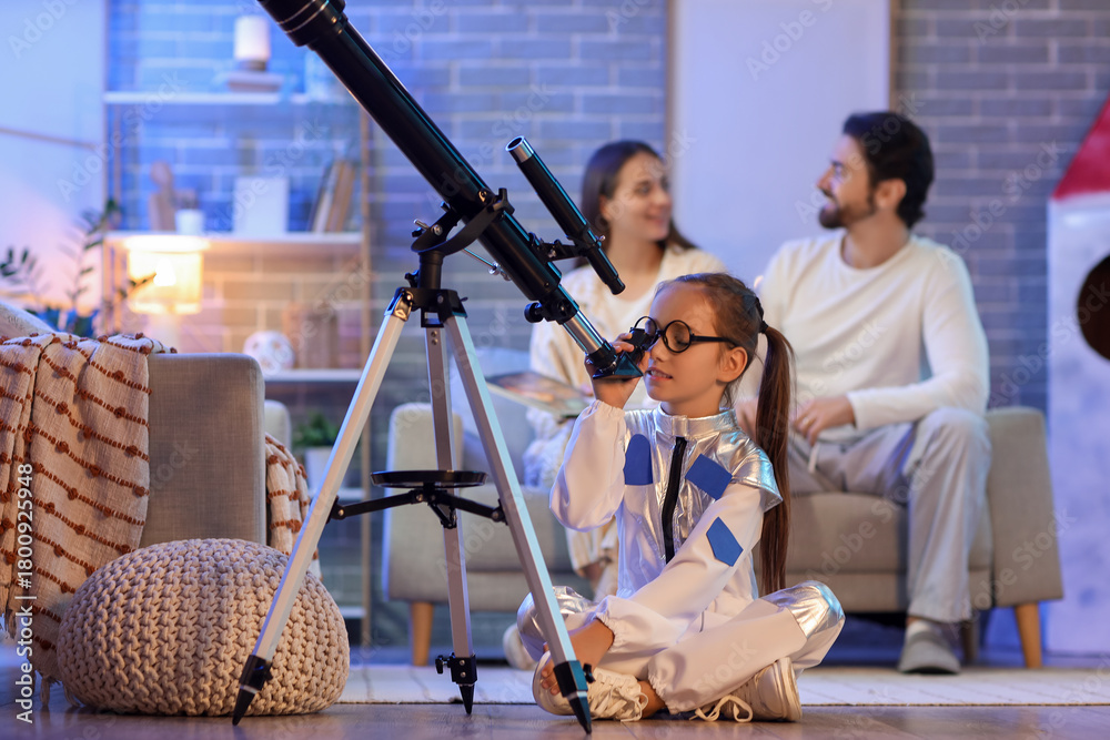 Fototapeta premium Little girl looking through telescope and her parents at home in evening