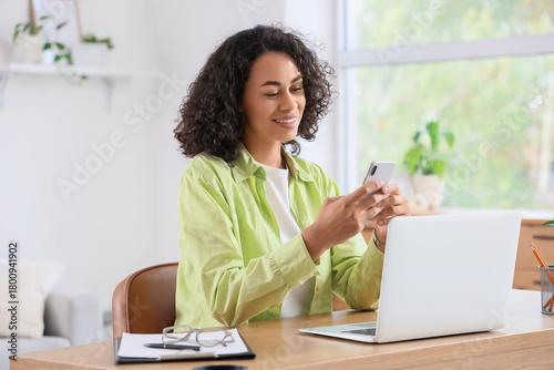 Foto Young African-American woman using mobile phone to search online at home
