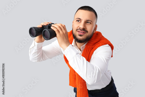 Young businessman with binoculars on light background. Search concept